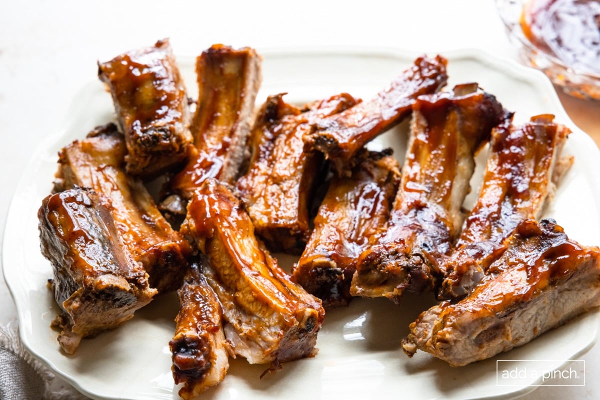 Photo of cooked ribs on a white platter with more bbq sauce on the side.