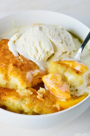 Photo of peach cobbler in a white bowl with vanilla ice cream