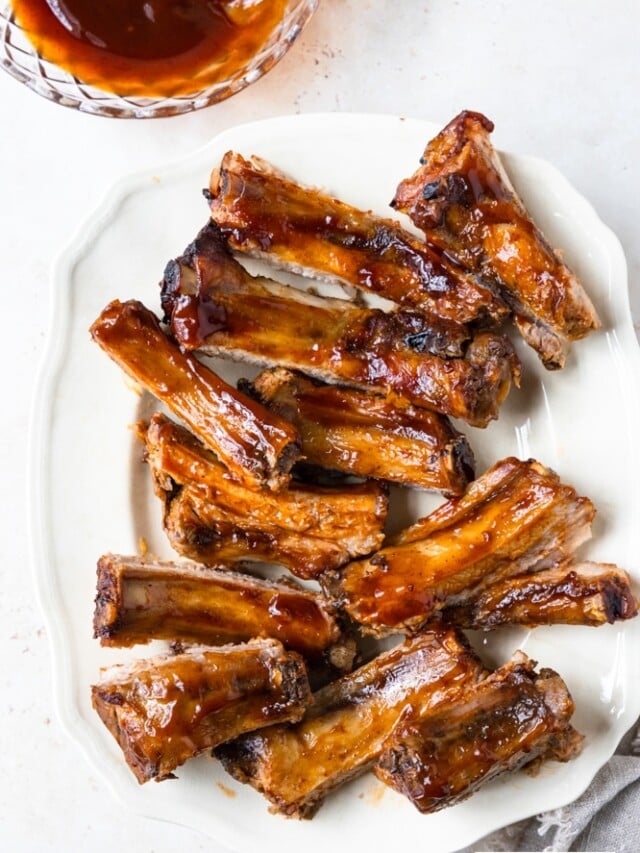 Photo of BBQ ribs on a white platter on a white background.