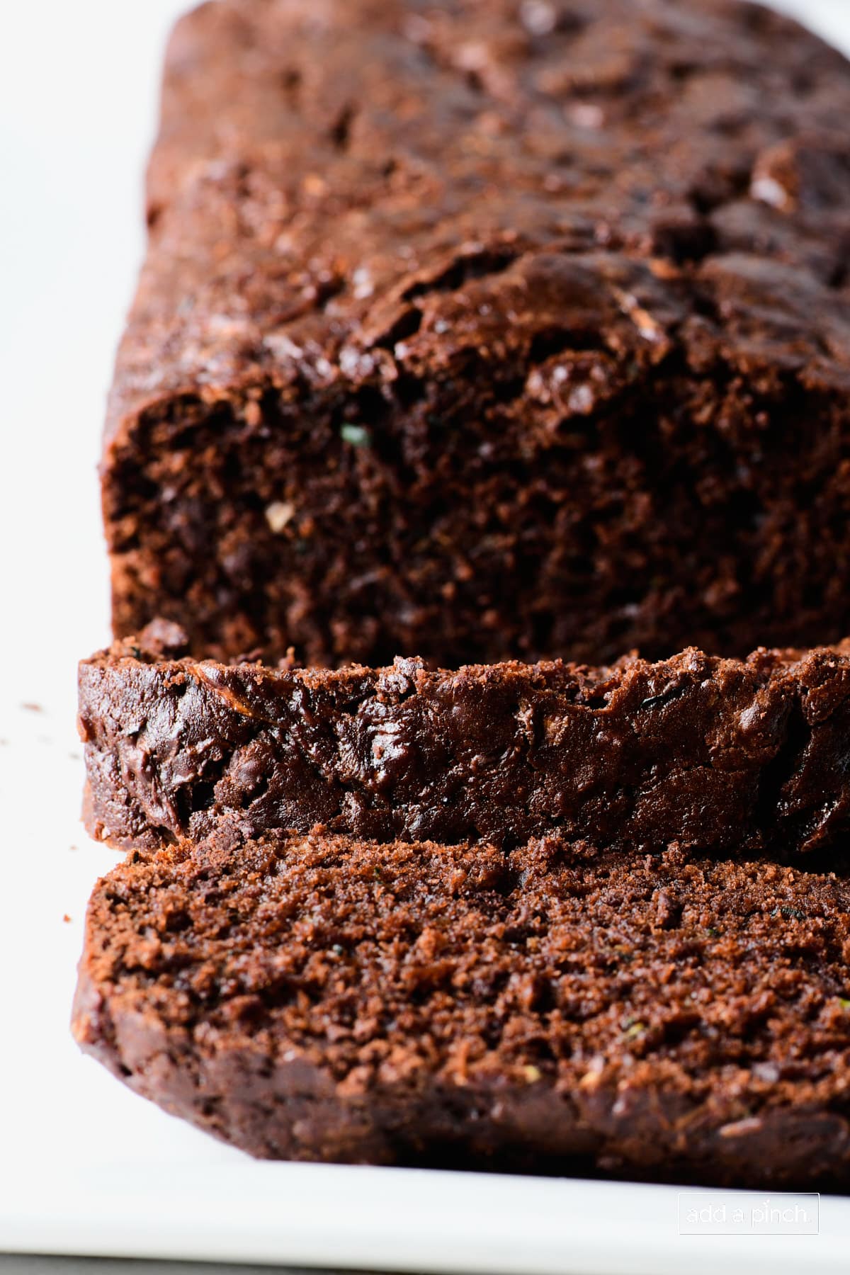 Partially sliced, chocolatey Chocolate Zucchini Bread on white platter.