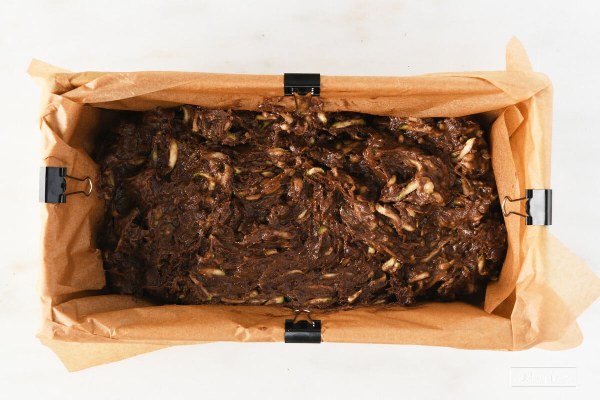 Unbaked chocolate zucchini bread in a loaf pan lined with parchment paper.