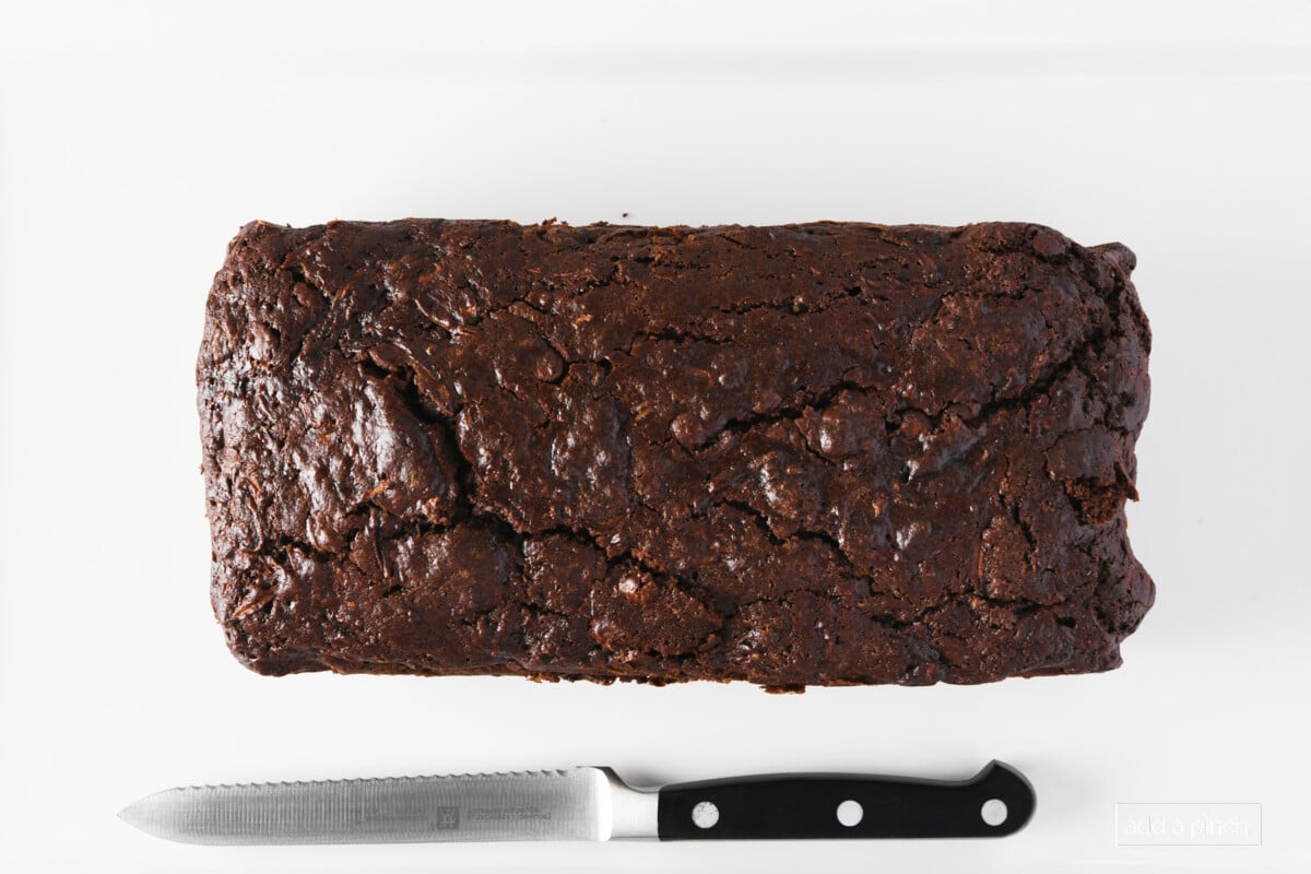 Baked chocolate zucchini bread on a white platter with a knife.
