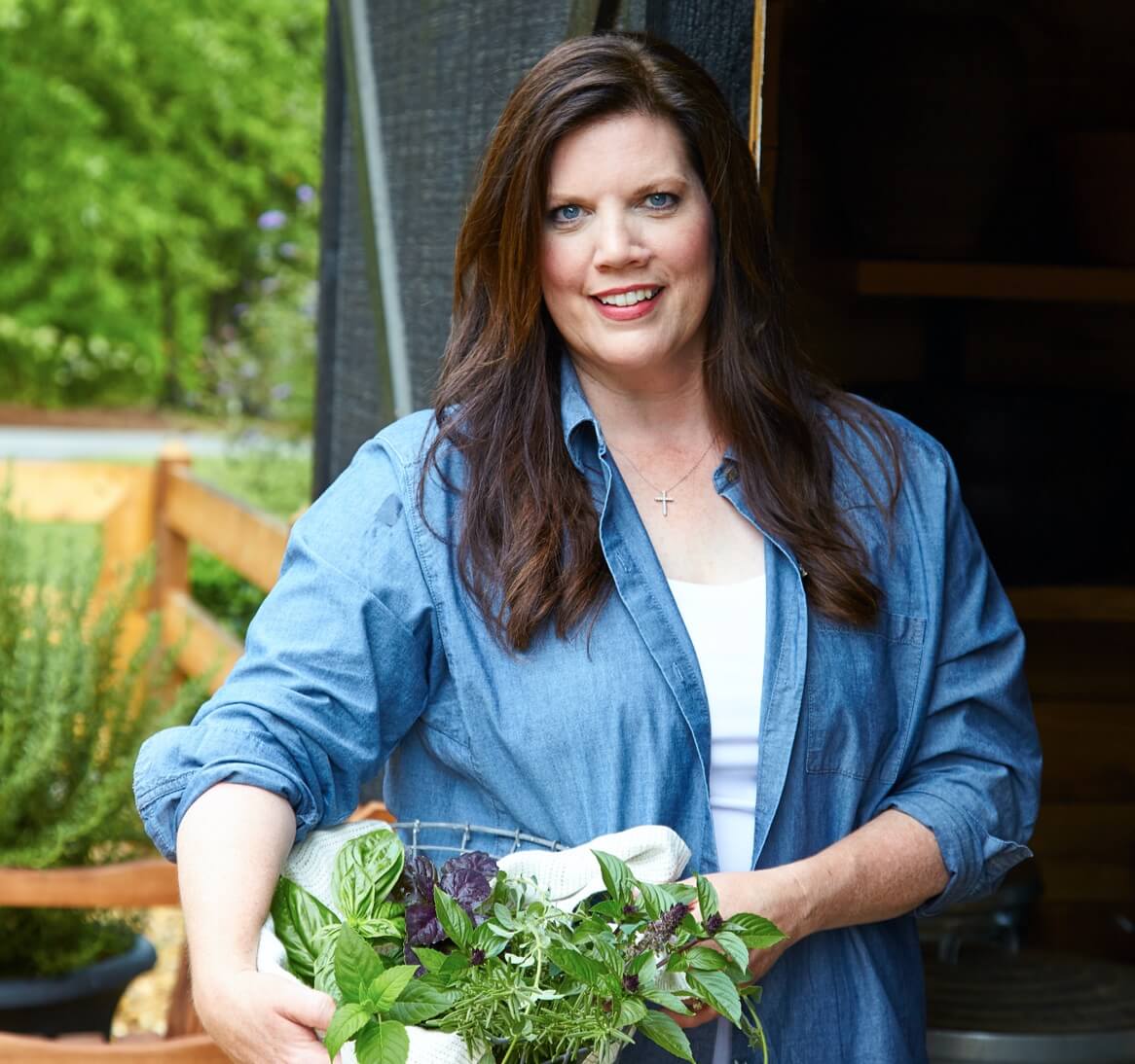 Photo of Robyn Stone holding fresh herbs at her kitchen garden potting shed.