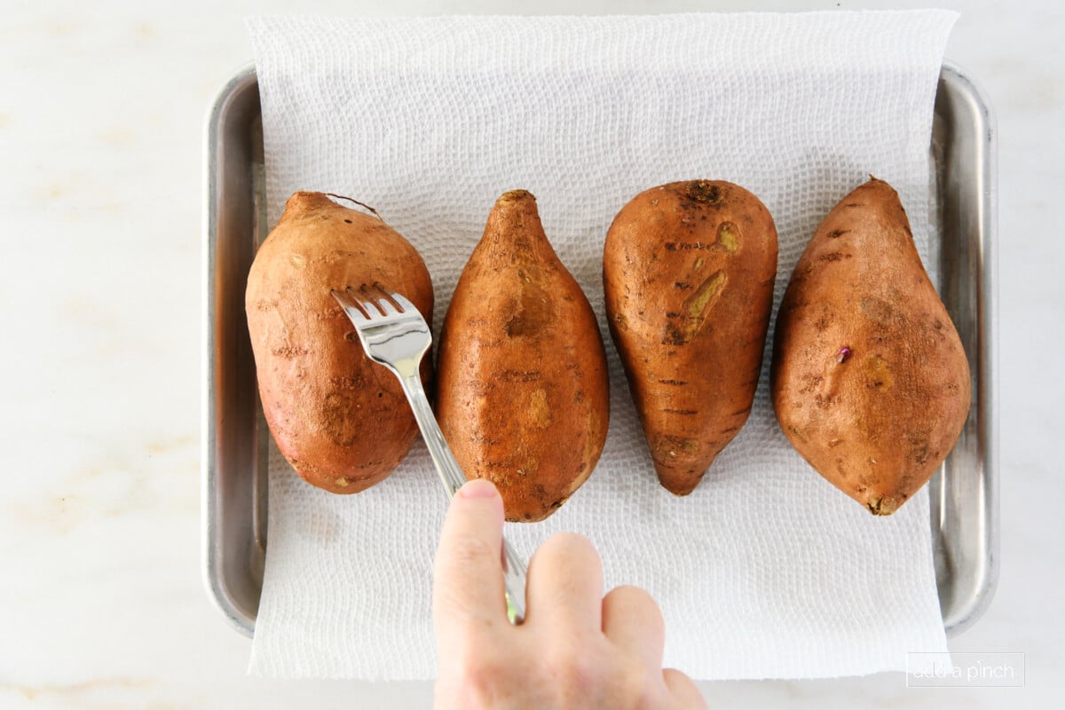 Sweet potatoes on a baking sheet with holes being pierced with a fork.