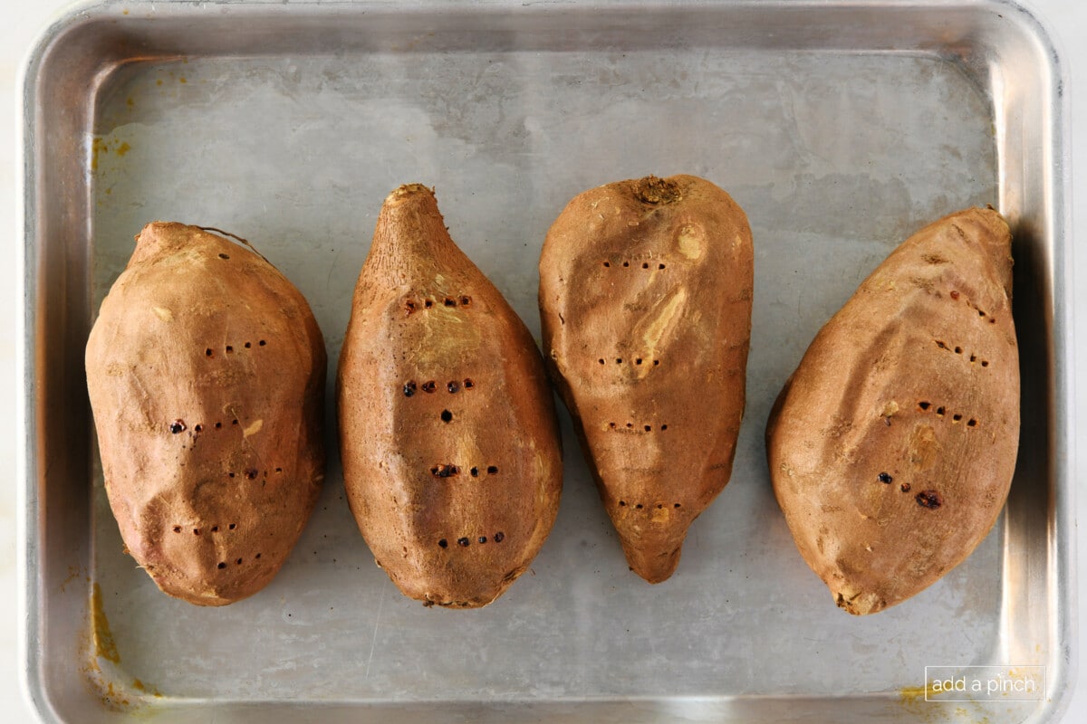 Four baked sweet potatoes on a baking sheet.