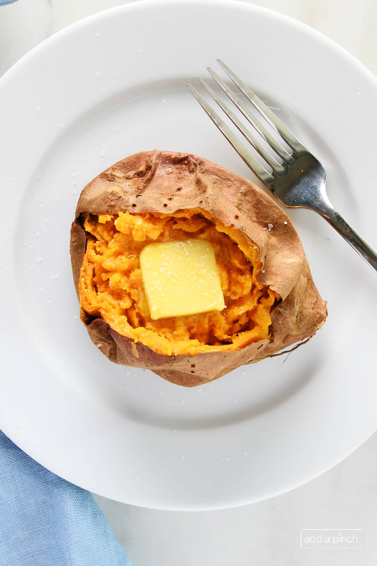 photo of baked sweet potato topped with butter and salt on a white plate with a fork.