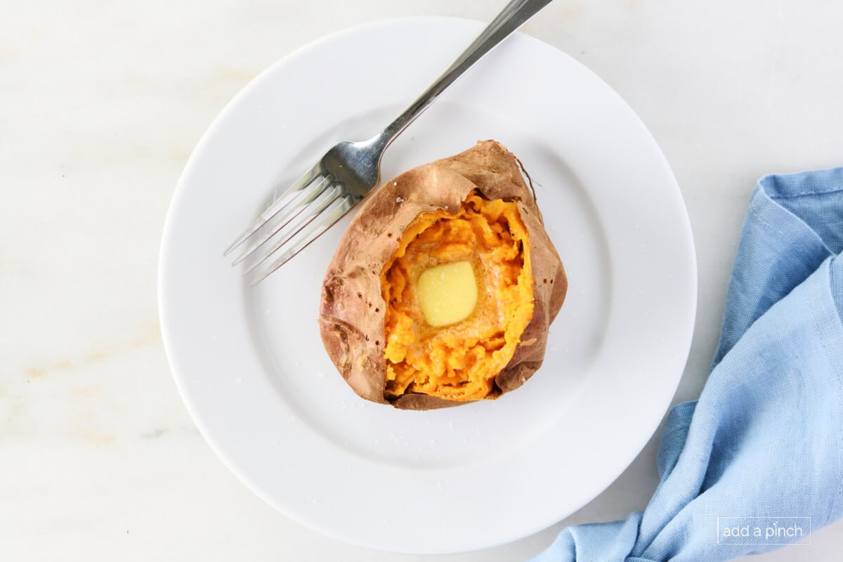 Baked sweet potato on a white plate with a fork topped with butter and salt.
