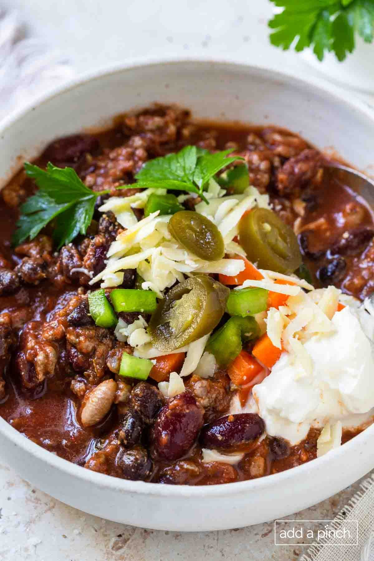Bowl of the best classic chili made with beef, beans, tomatoes and spices and then topped with your favorite toppings. Photographed in a white bowl with garnish on a white surface.// addapinch.com