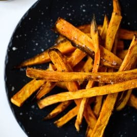 Photograph of sweet potato fries on a black plate on a white background.