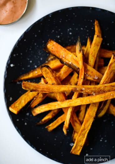 Photograph of sweet potato fries on a black plate on a white background.