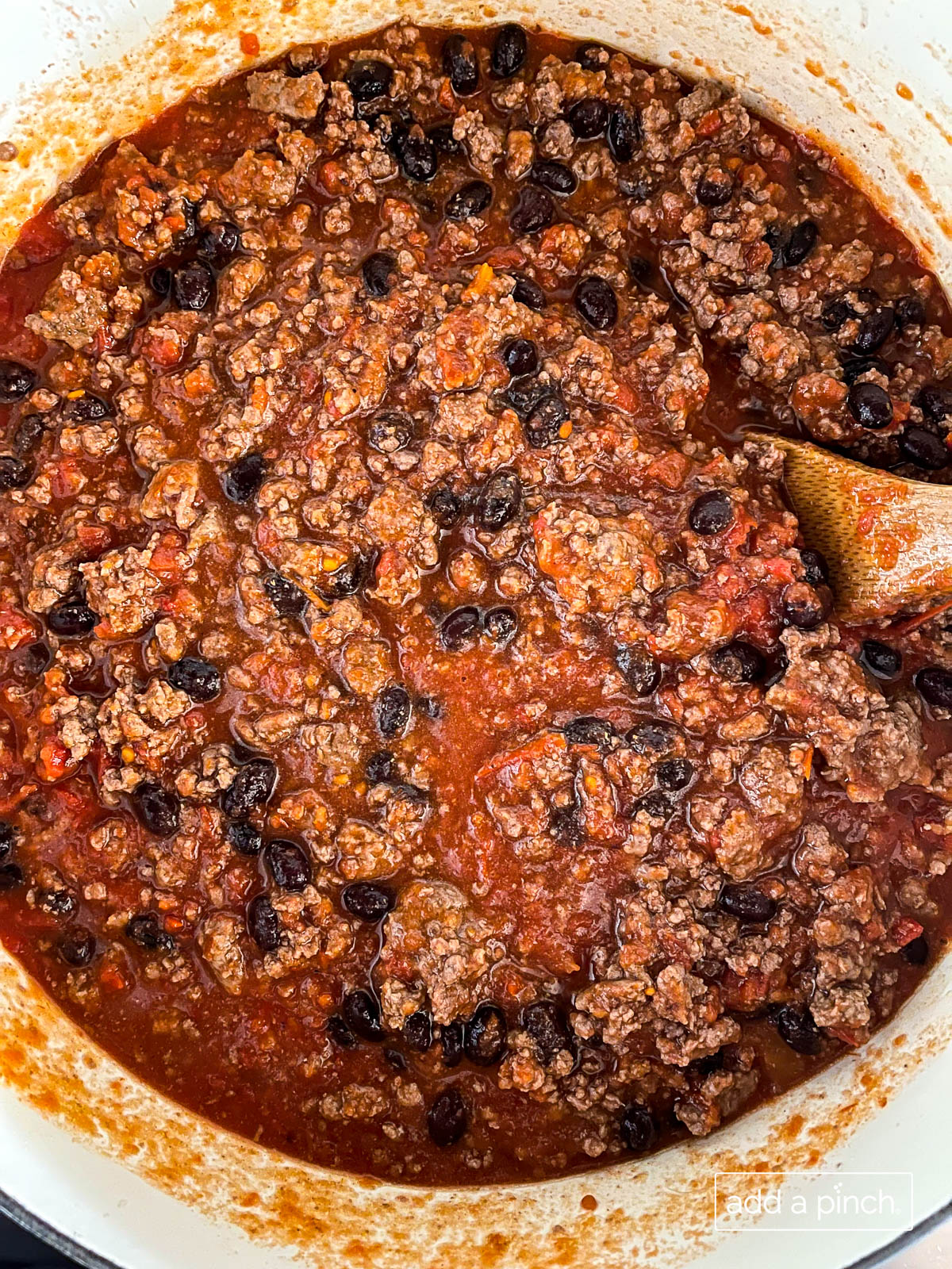 Overhead photograph of chili in a white dutch oven with a wooden spoon. 