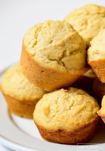 Closeup photograph of stack of cornbread muffins on a white background.
