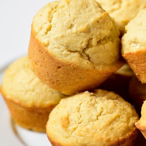 Closeup photograph of stack of cornbread muffins on a white background.
