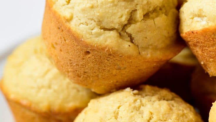 Closeup photograph of stack of cornbread muffins on a white background.