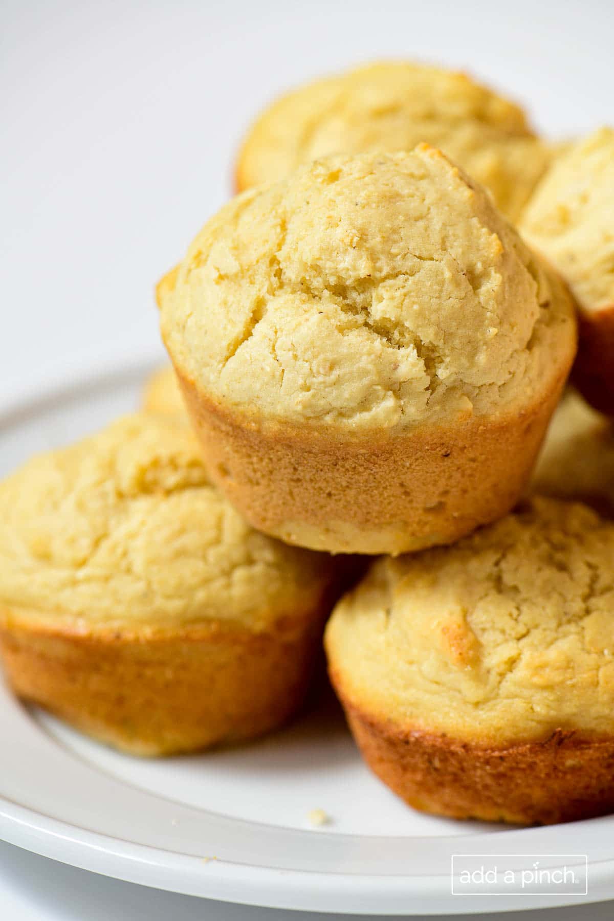 Closeup photo of stack of cornbread muffins on a white plate and white background. 