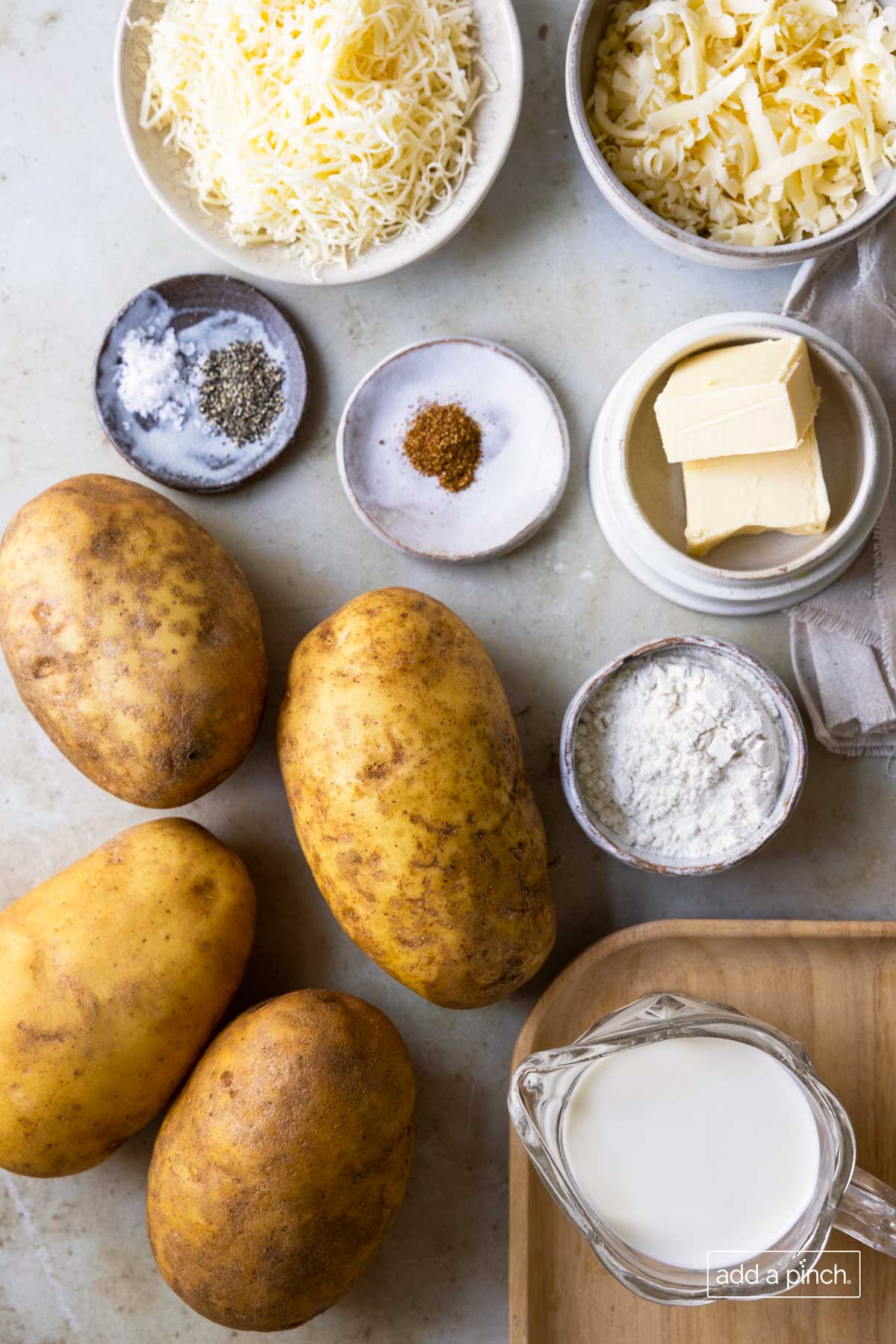 Photograph of potatoes, flour, butter, seasonings, milk and shredded cheese ready to be used to make a potato side dish.
