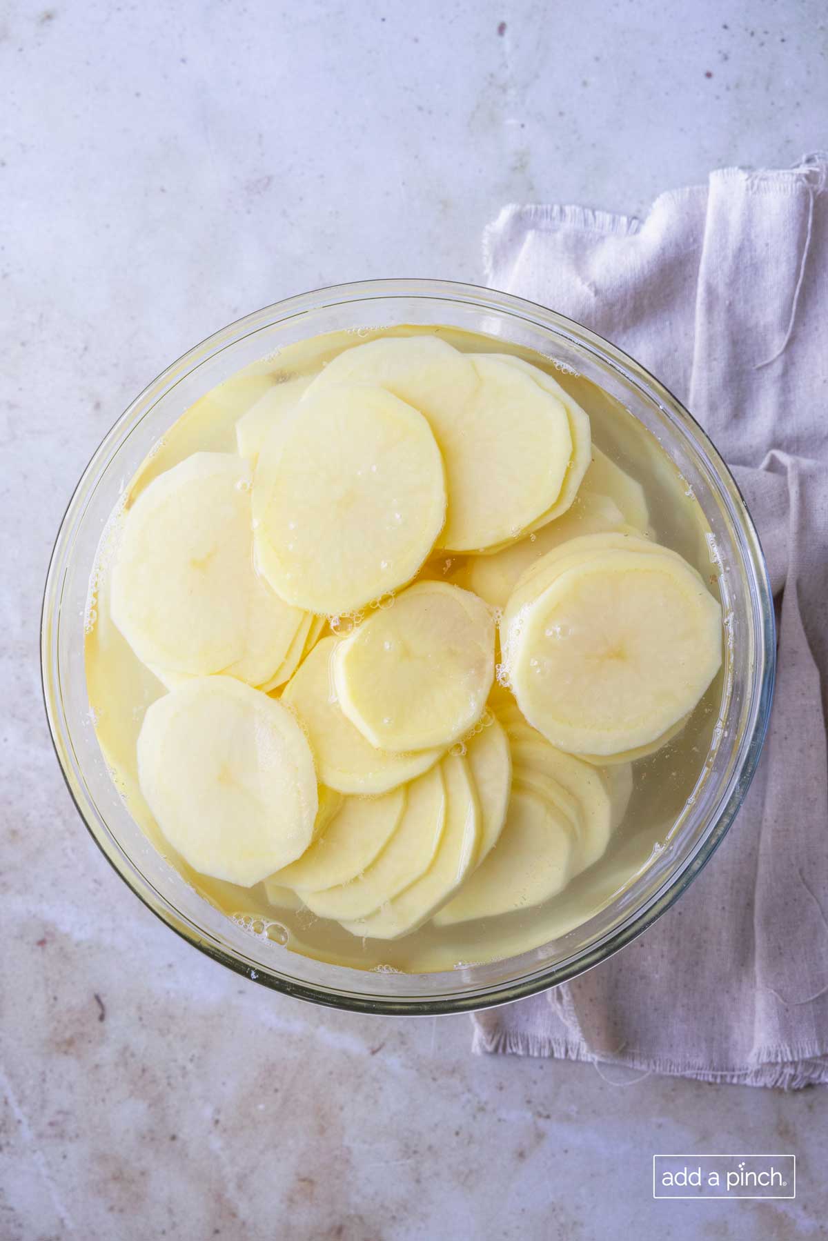 Photo of sliced potatoes in a glass bowl filled with water.