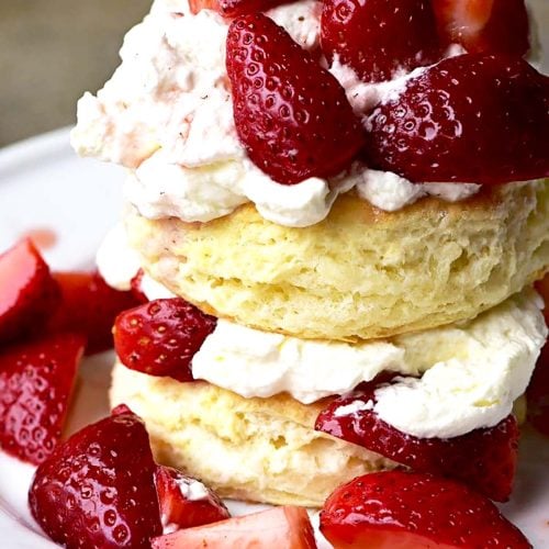 Strawberry shortcake with layers of homemade whipped cream and fresh sliced strawberries on a white plate. // addapinch.com