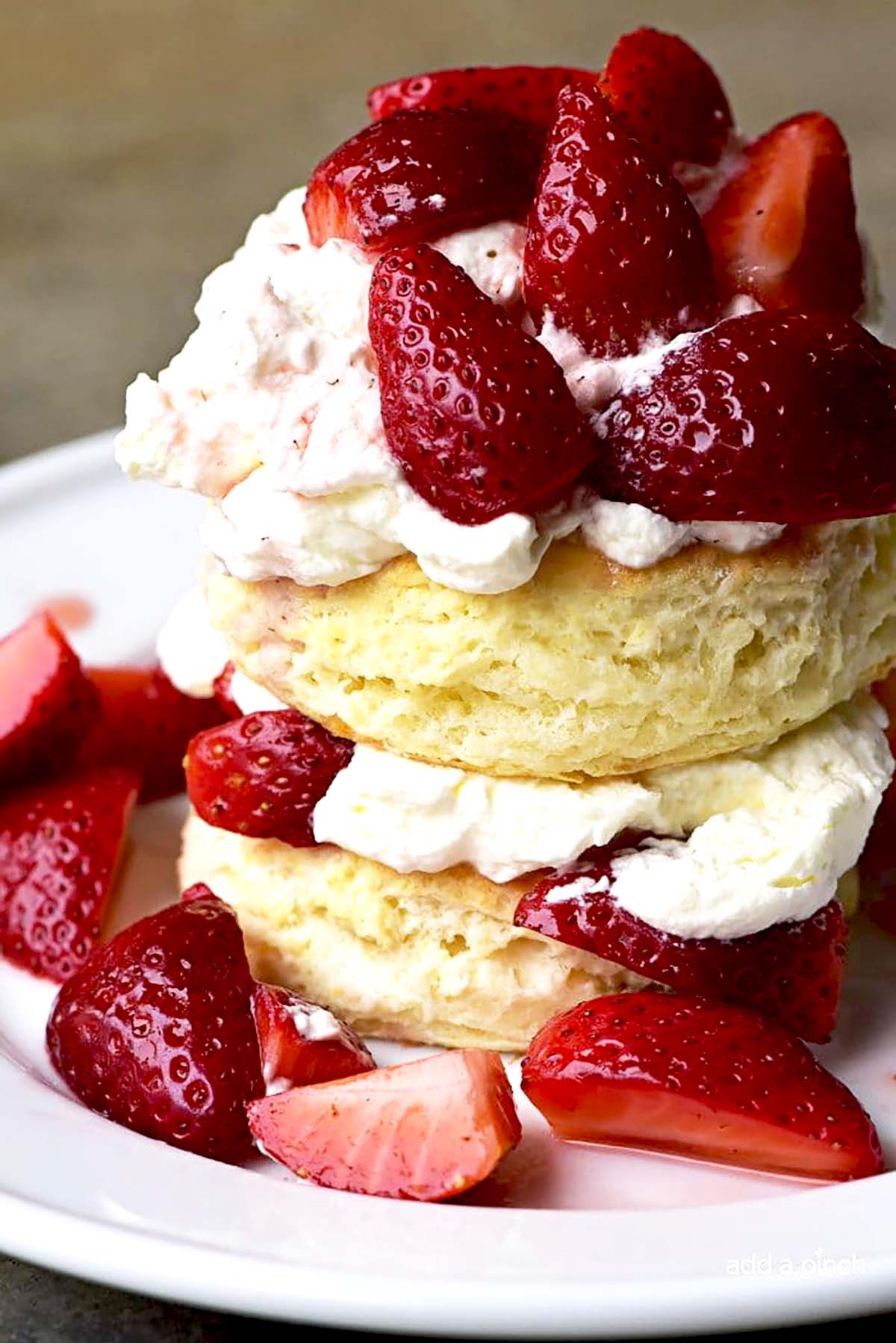 Strawberry shortcake with layers of sliced strawberries and whipped cream on a white plate on a brown background.