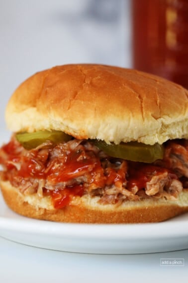 Photograph of pulled pork on a bun with bbq sauce and pickles. // addapinch.com