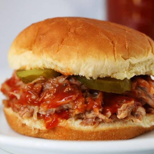 Photograph of pulled pork on a bun with bbq sauce and pickles. // addapinch.com