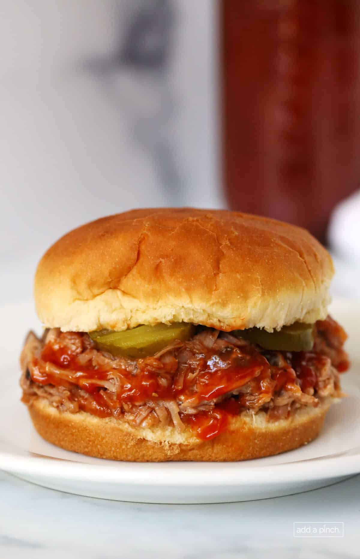 Photograph of pulled pork sandwich with additional bbq sauce and pickles. // addapinch.com