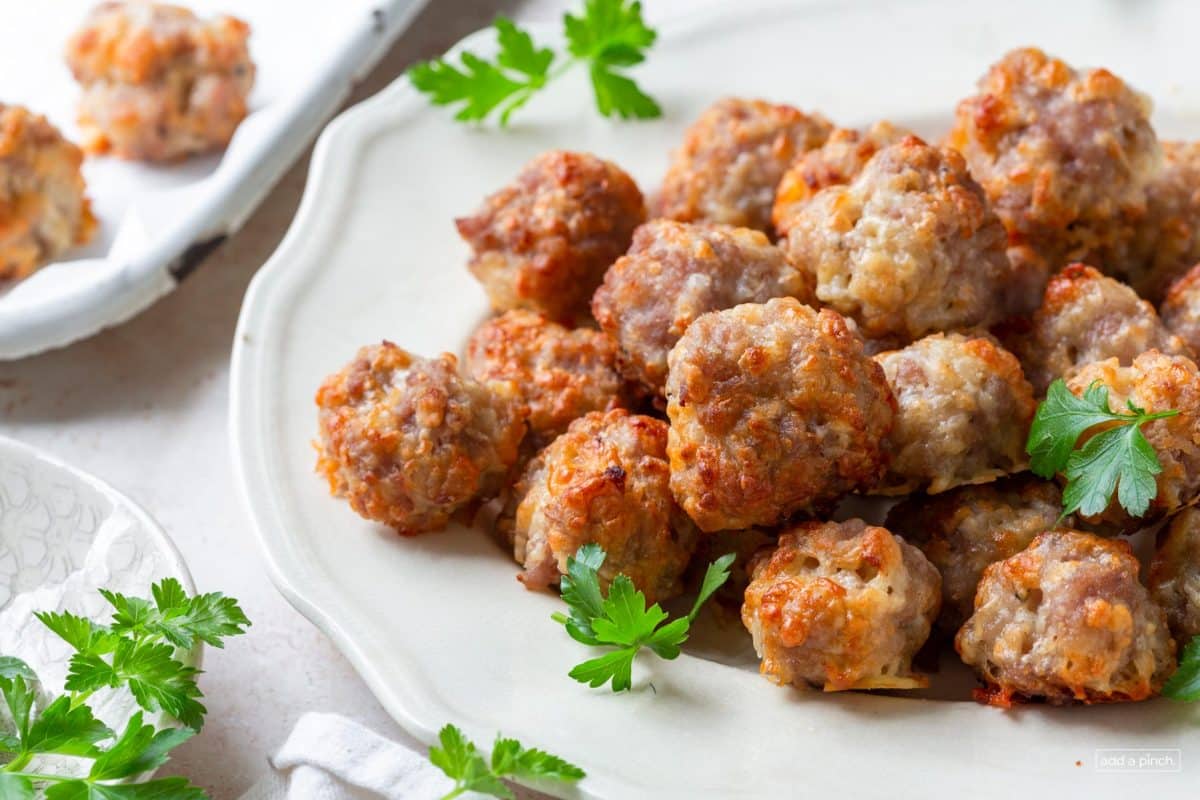 Photo of sausage balls on a white serving platter with green garnish.