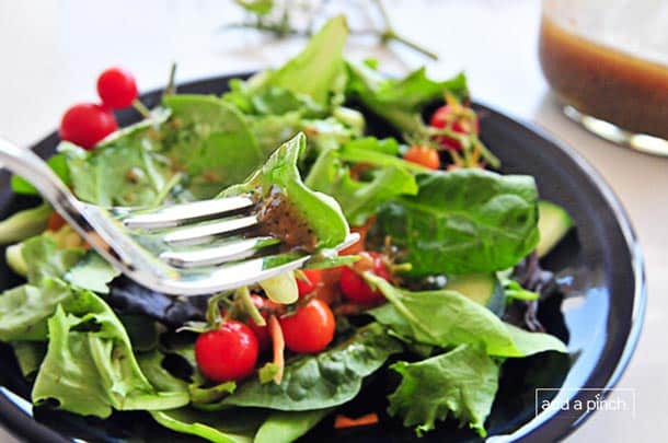 Photograph of plate filled with salad greens, tomatoes, avocado, parmesan cheese and a piece of spinach on a fork with dressing.