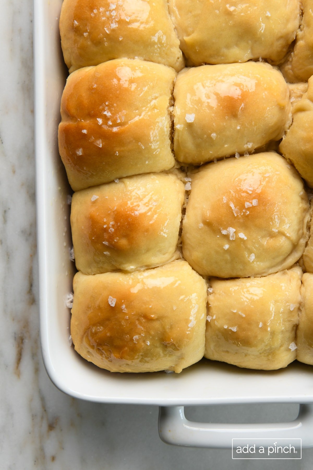 Photo of buttery dinner rolls in a white baking dish on a marble counter.