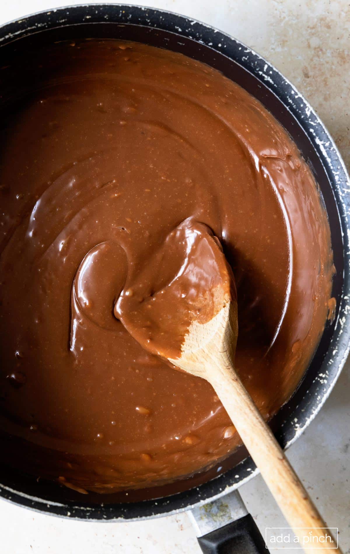Photo of melted chocolate in a saucepan  with a wooden spoon ready to be poured into a prepared pan.
