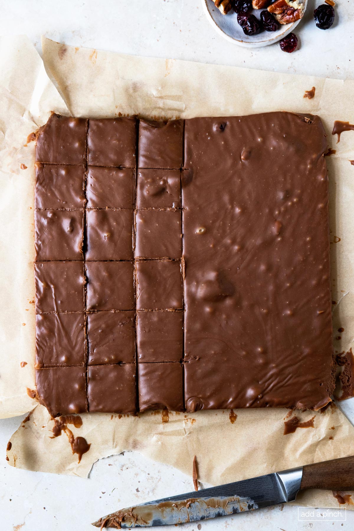 Image of block of chocolate fudge on a piece of parchment being cut into individual pieces.