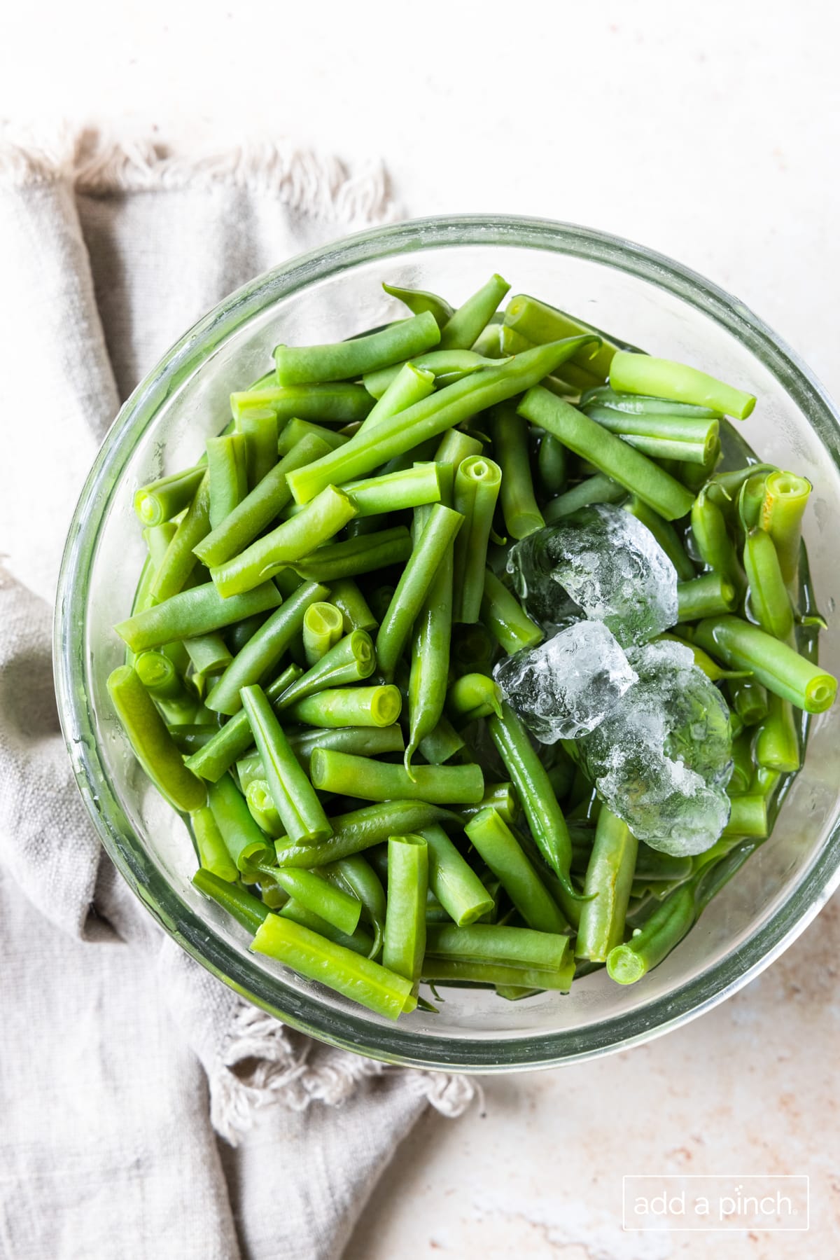 Fresh green beans in a glass bowl with ice.