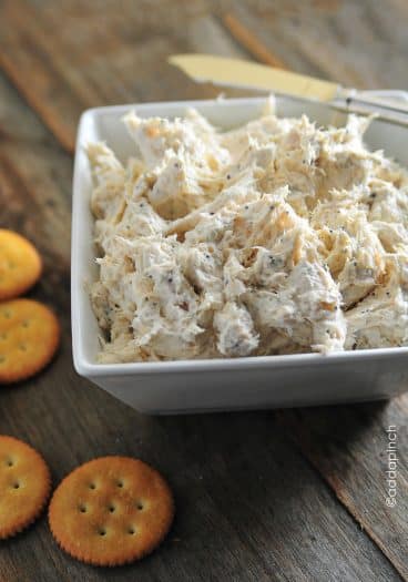 Image of poppy seed chicken dip in a white bowl with crackers around the bowl. All placed on a wooden surface.