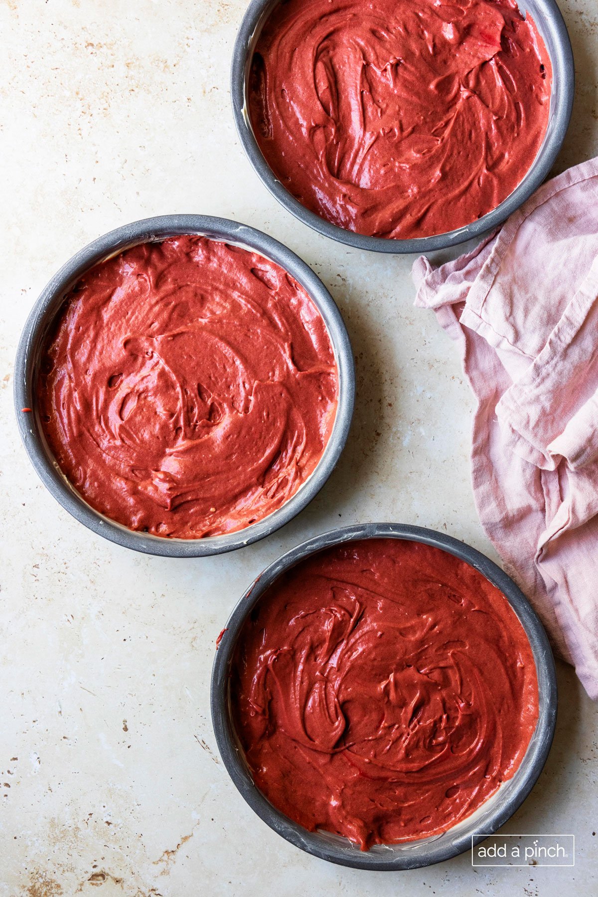 Photograph of red velvet cake batter evenly distributed in three cake pans.