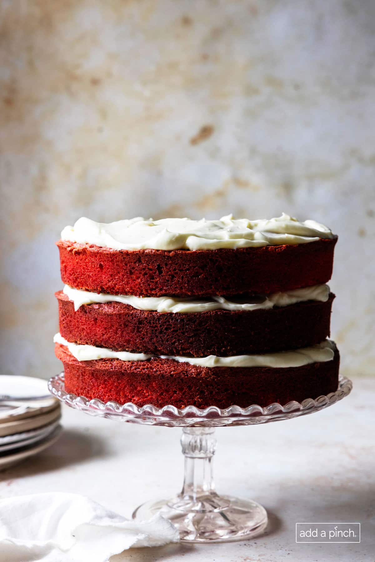 Photograph of three layered red velvet cake with white fluffy frosting in between the layers.