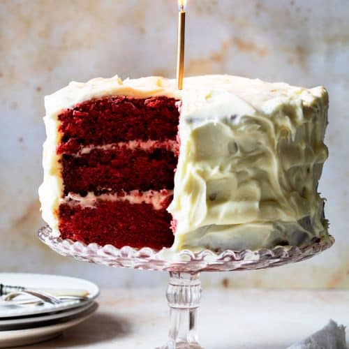 Image of red velvet cake with a lit gold candle.