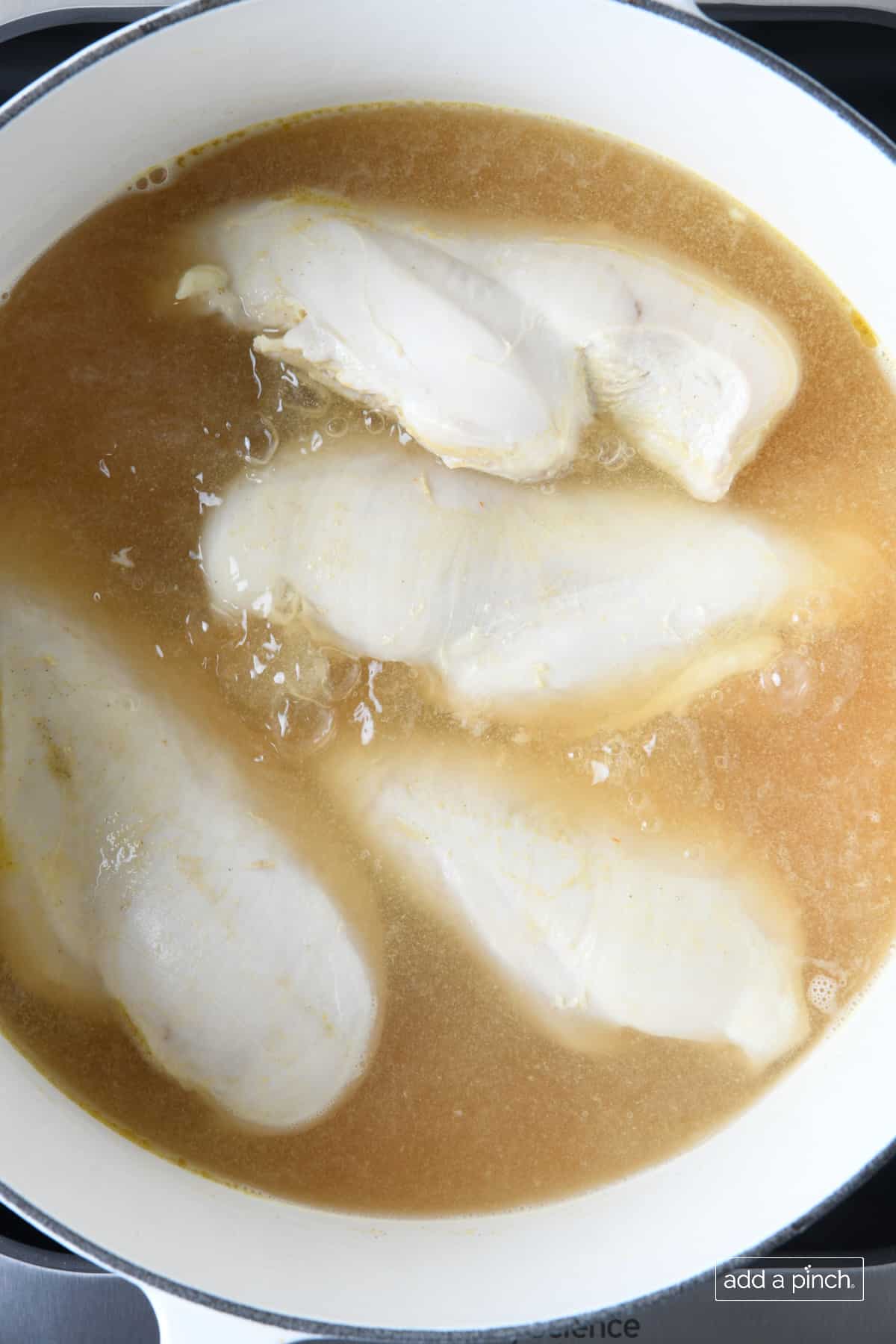Chicken breast and chicken stock simmering in a white Dutch oven.