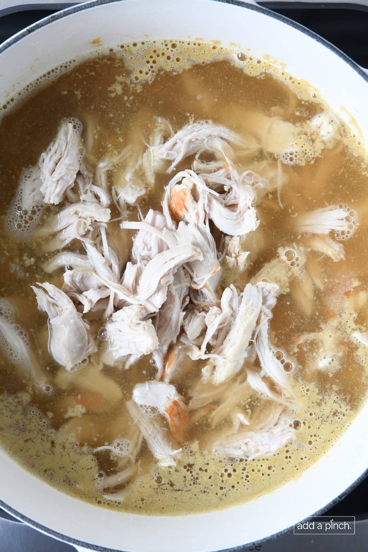 Shredded chicken and chicken stock simmering in a white Dutch oven.