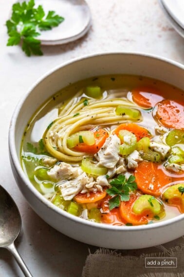 Photo of homemade chicken noodle soup in a white bowl on a white surface.