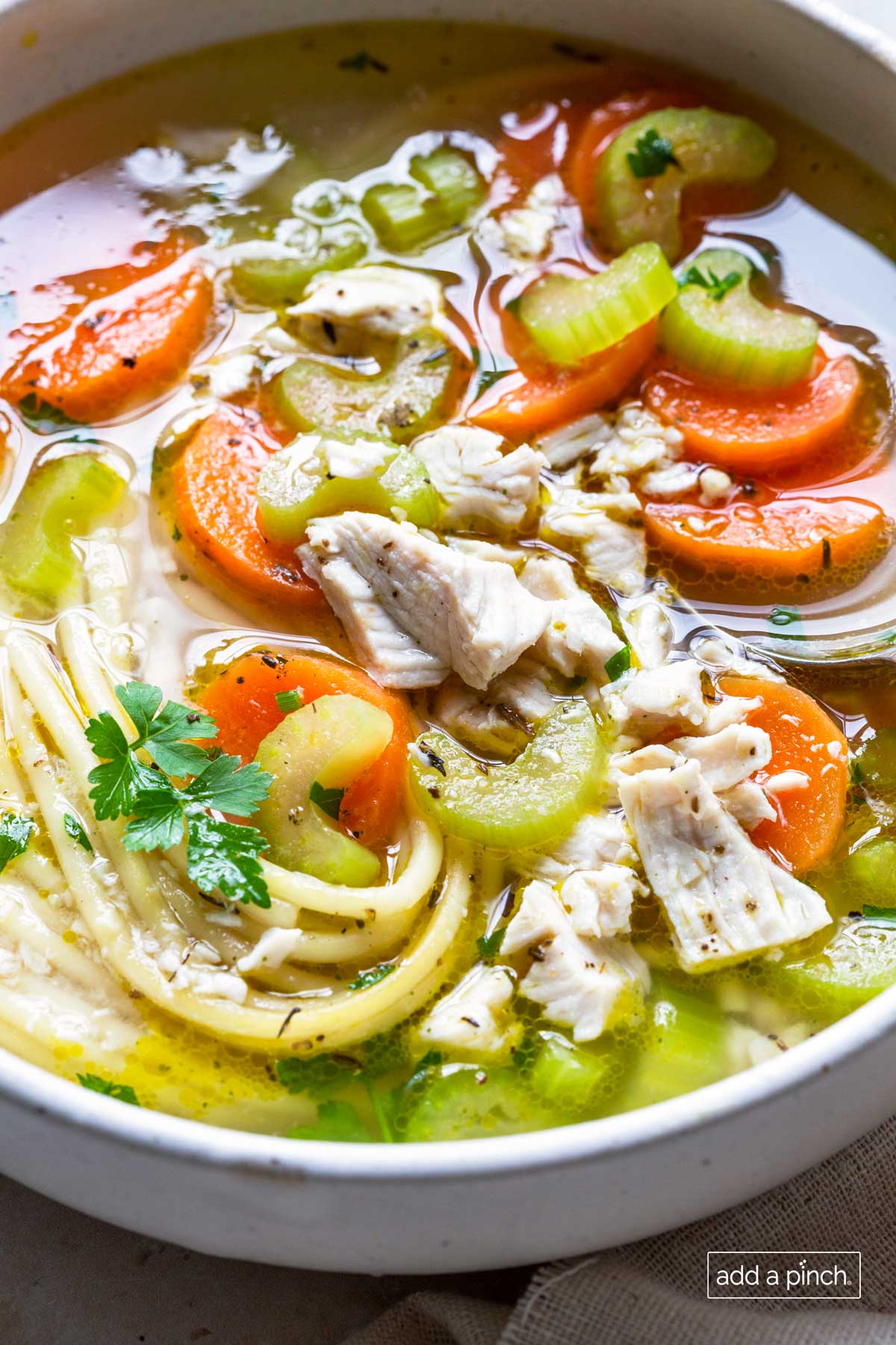 Close up photograph of chicken noodle soup in a white bowl.
