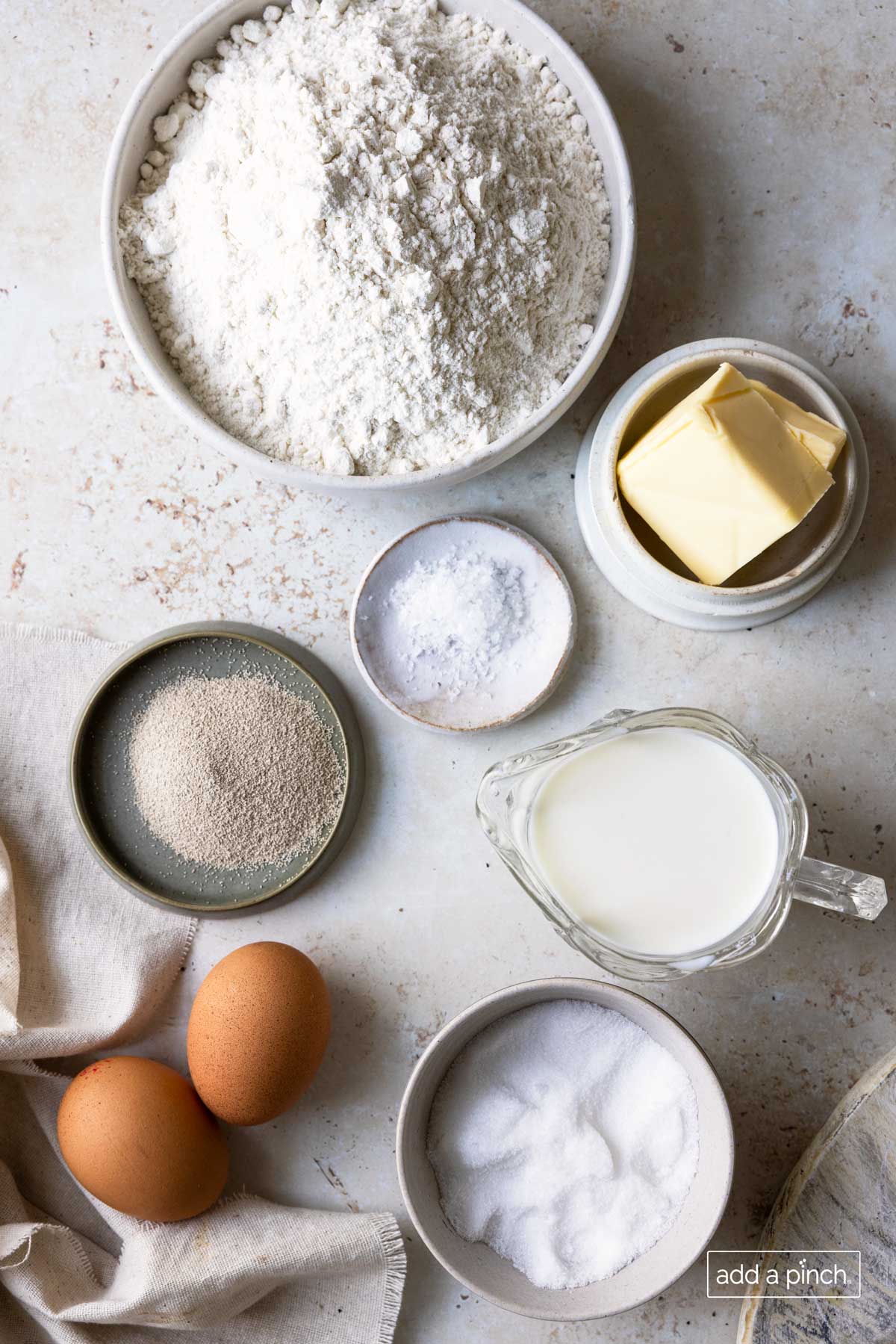 Marble countertop holds containers of ingredients for Cinnamon Roll recipe -  flour, yeast, butter, cinnamon, sugar, eggs, salt, and milk. 
