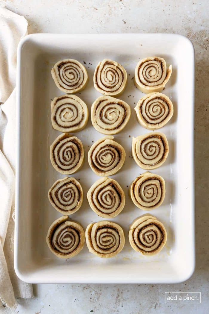 Photo of sliced cinnamon roll in a white baking dish ready to rise.