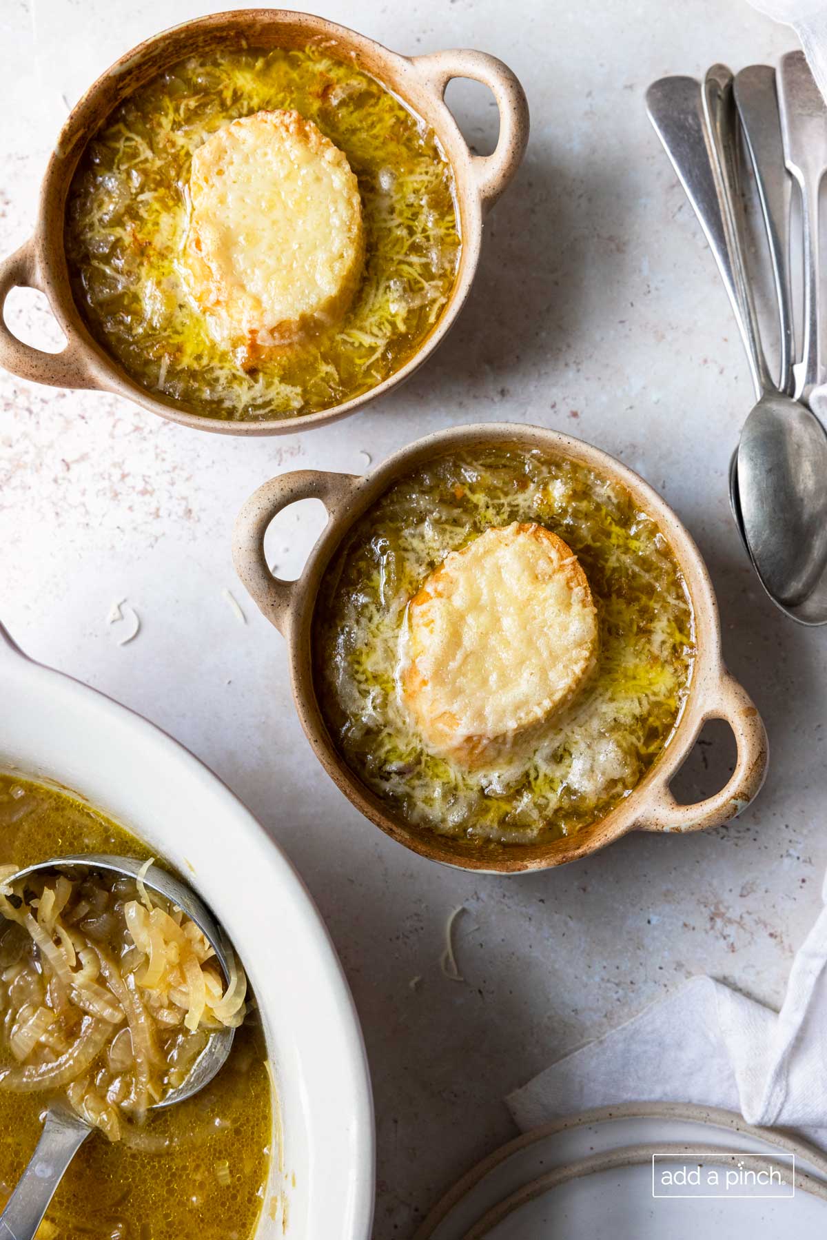 Soup crocks hold french onion soup that has slice of crusty bread topped with melted cheeses.