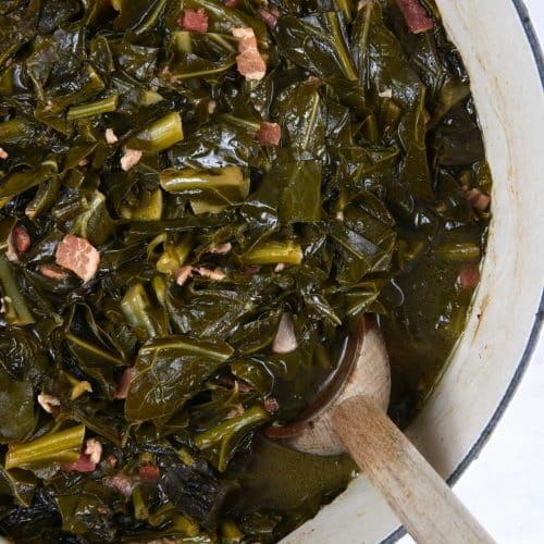 Photo of white pot filled with cooked collard greens and a wooden spoon.