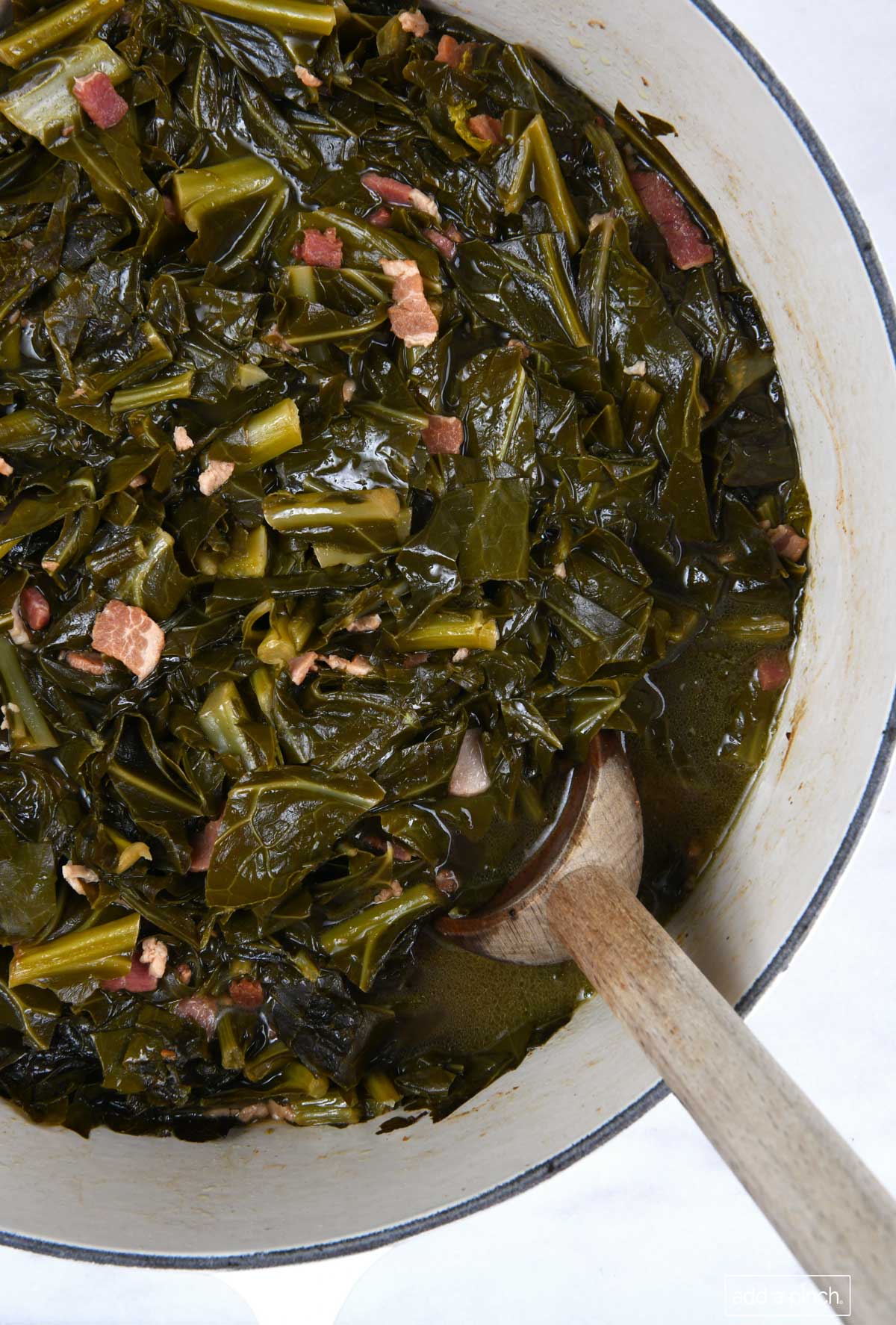 Photo of pot filled with cooked collard greens with a wooden spoon.