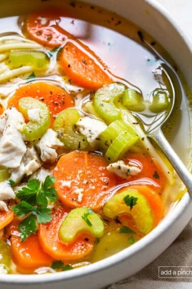 Photo of a bowl of chicken noodle soup in a white bowl with a spoon.