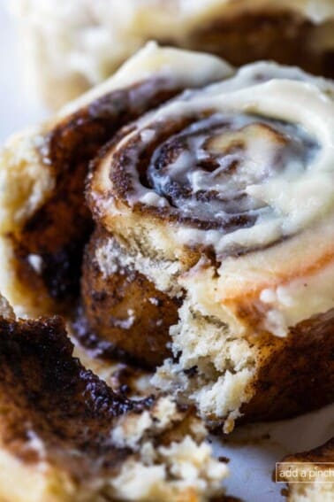 Photograph of cinnamon rolls with cream cheese frosting on a white plate with the inside with gooey cinnamon roll filling showing.