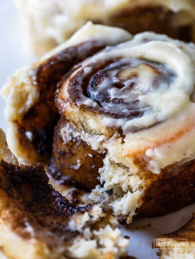Photograph of cinnamon rolls with cream cheese frosting on a white plate with the inside with gooey cinnamon roll filling showing.
