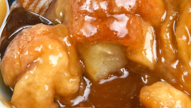 Photo of white bowl filled with baked apple dumplings topped with vanilla ice cream and caramel sauce.