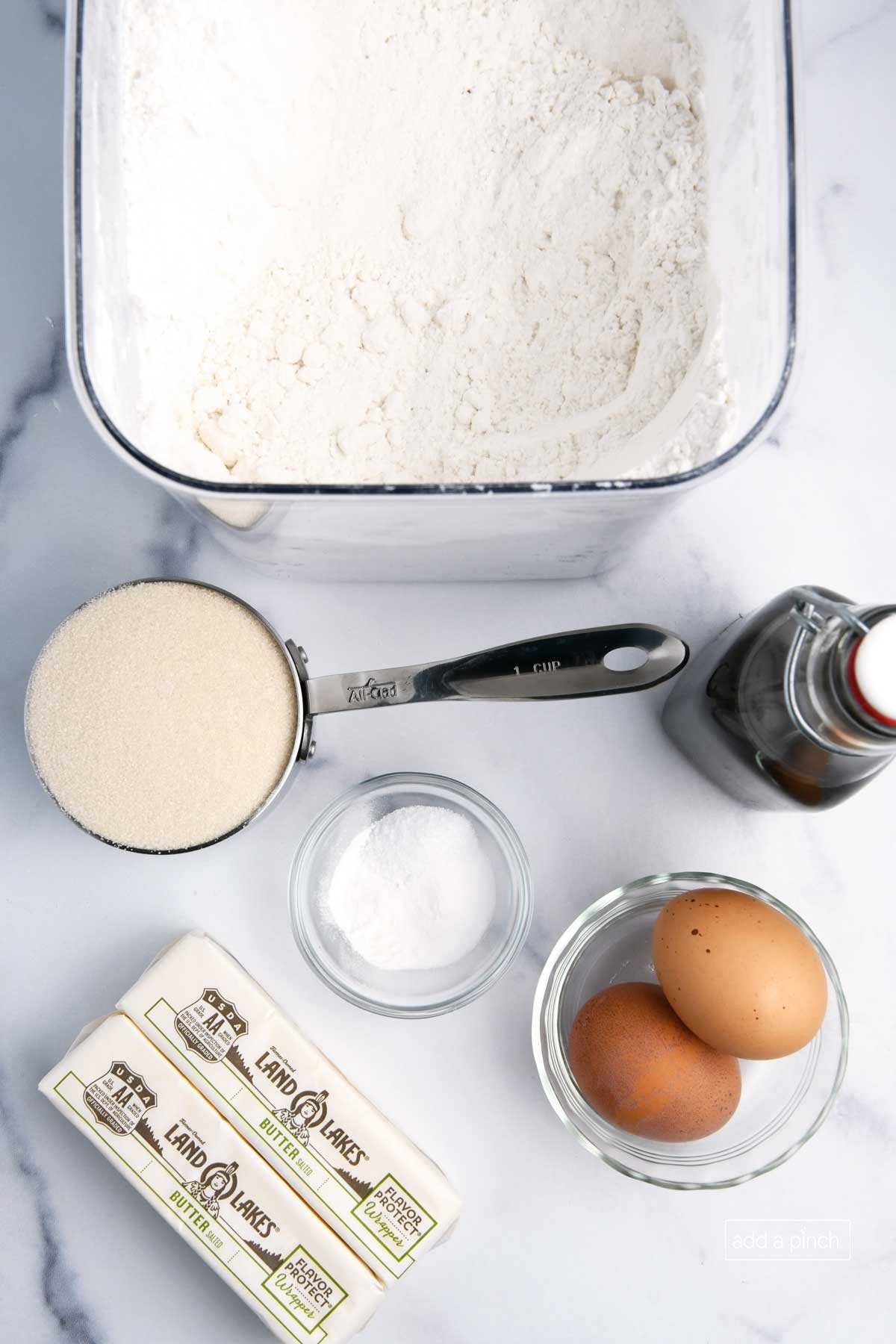 Photograph of ingredients used to make rolled sugar cookies: flour, sugar, vanilla extract, eggs, and butter.